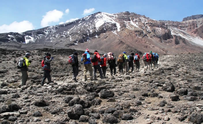 Climbers traversing the high-altitude volcanic terrain with Kilimanjaro's snow-capped peak in view